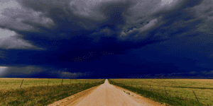 a long road stretching through country side below dark clouds